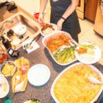 a group of people standing around a table filled with food