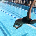 woman in black one piece swimsuit jumping on swimming pool during daytime