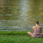 woman in brown tube dress sitting on green grass field near body of water during daytime