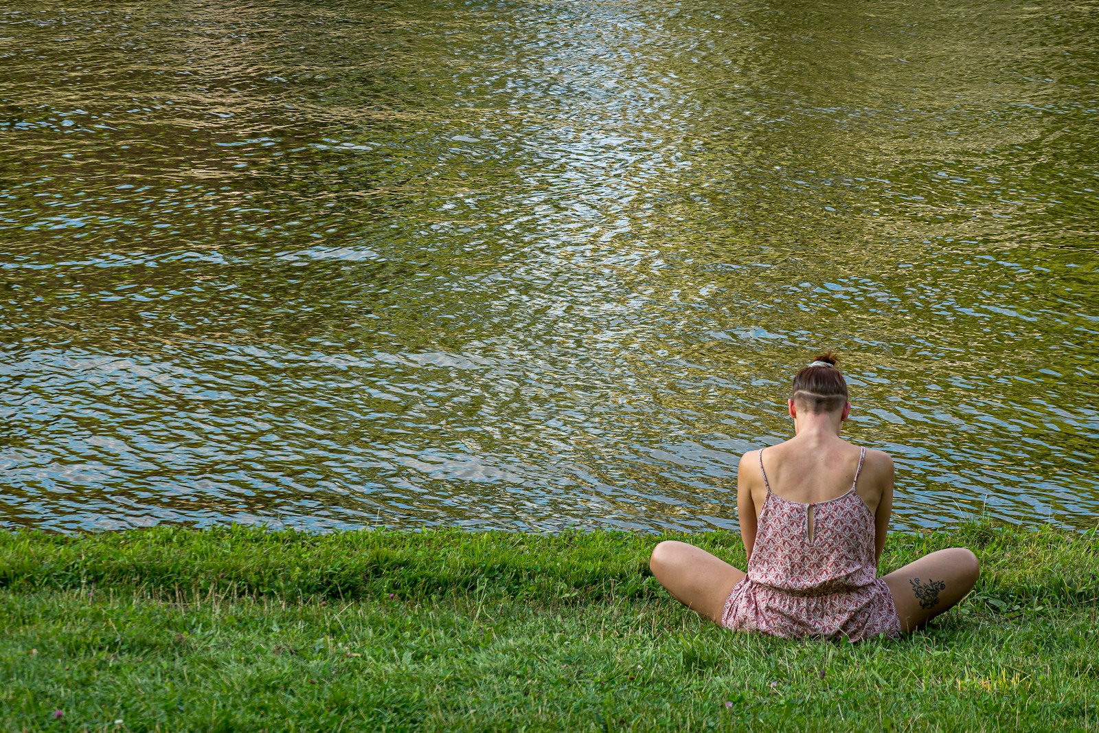 woman in brown tube dress sitting on green grass field near body of water during daytime