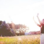 woman hands up in front of green meadows